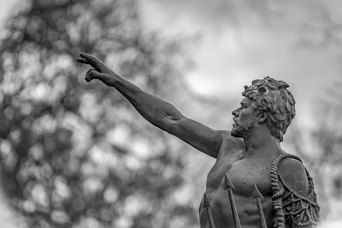 Weathered stone statue pointing upward in black and white